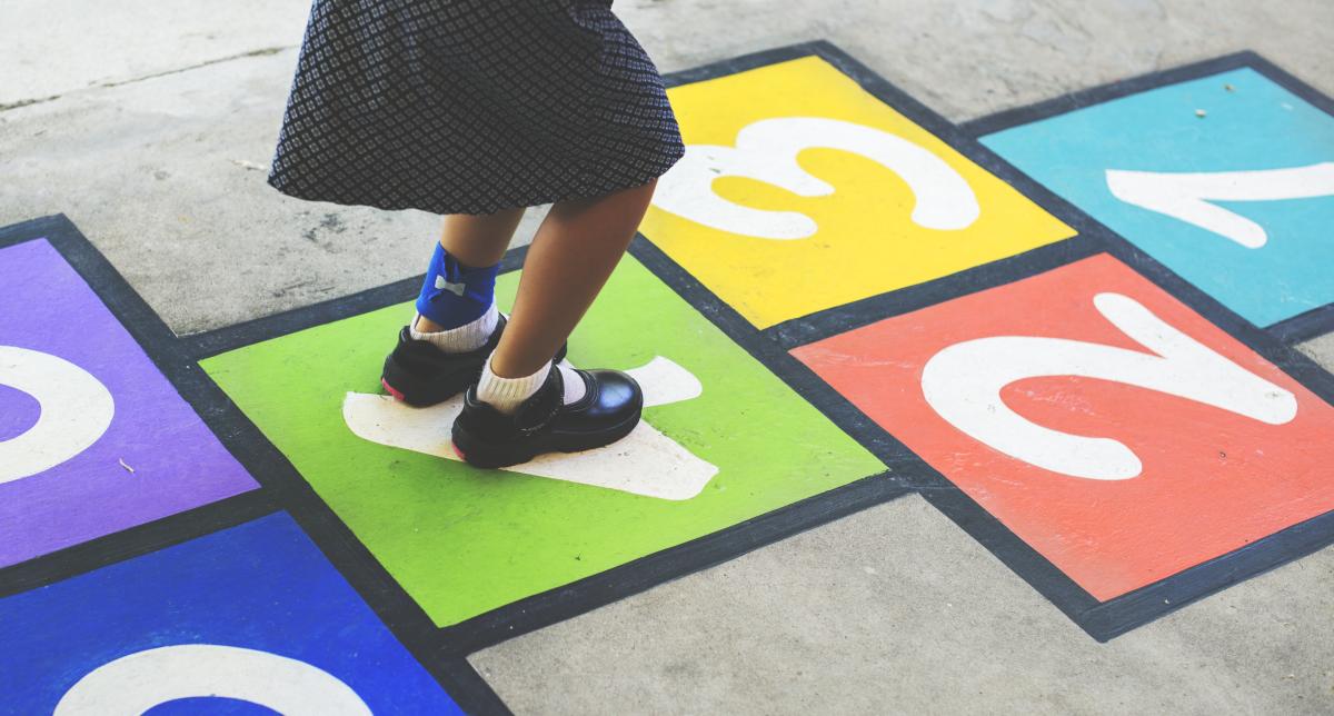 Girl in skirt playing hopscotch outside.