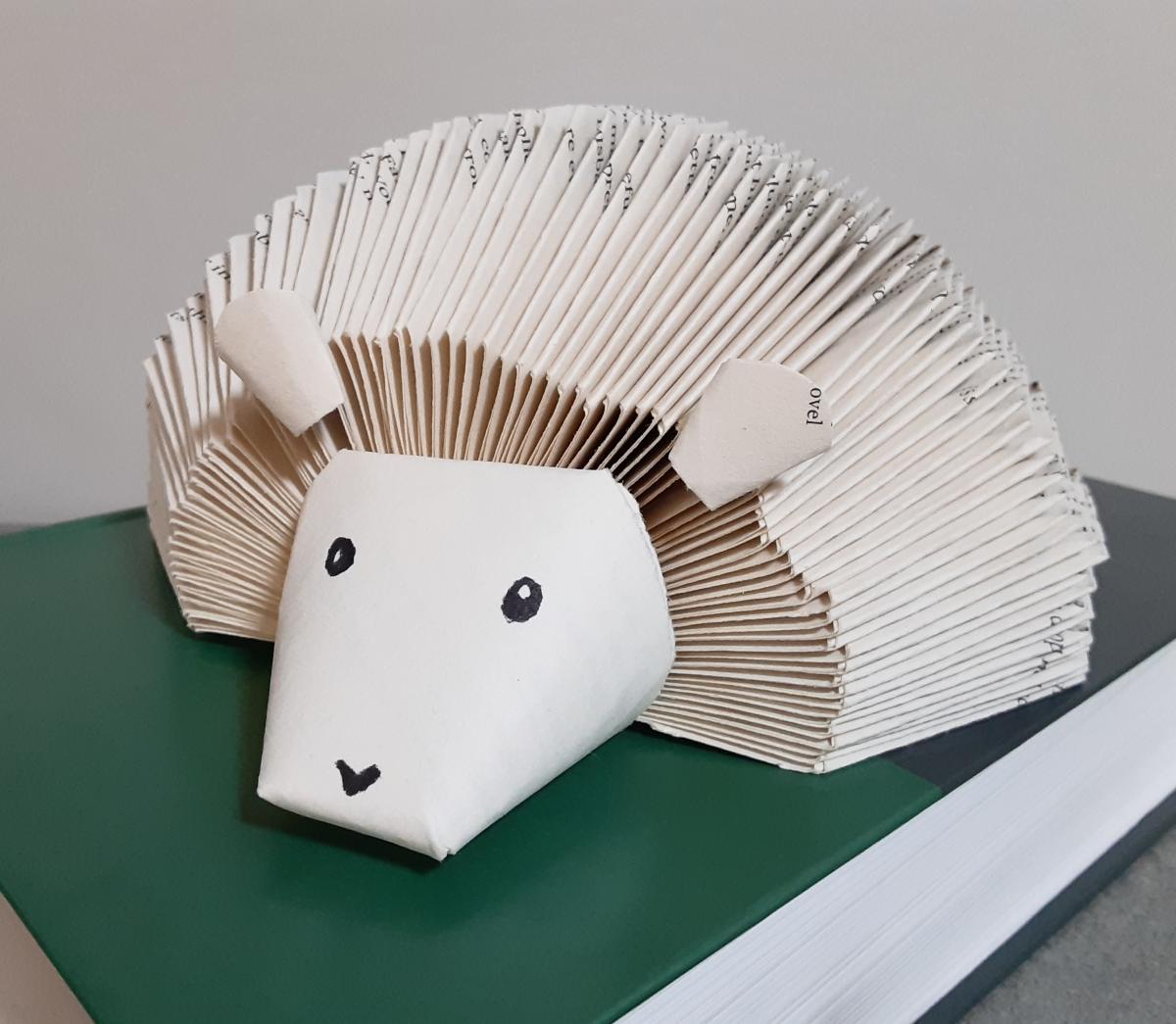 A paper hedgehog made out of book pages sitting on a book with a green cover.