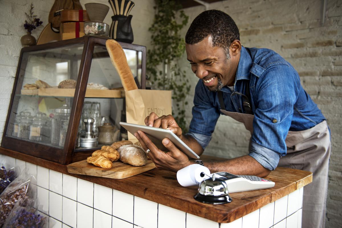 A man in a blue shirt leaning on a counter using a tablet.