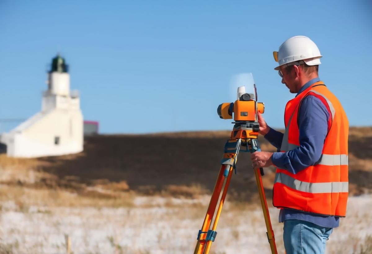 Man with hard hat and safety vest using survey equipment.