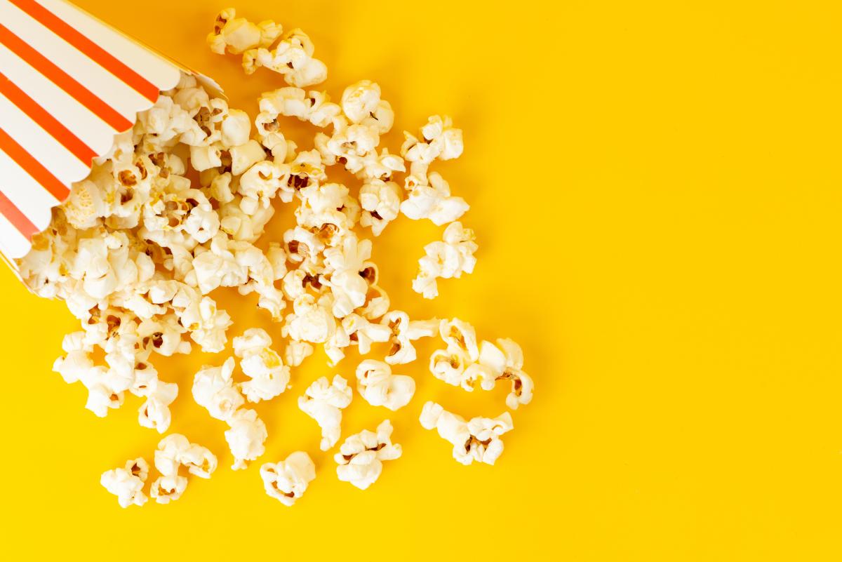 Tipped over red and white popcorn bucket with popcorn pouring out.