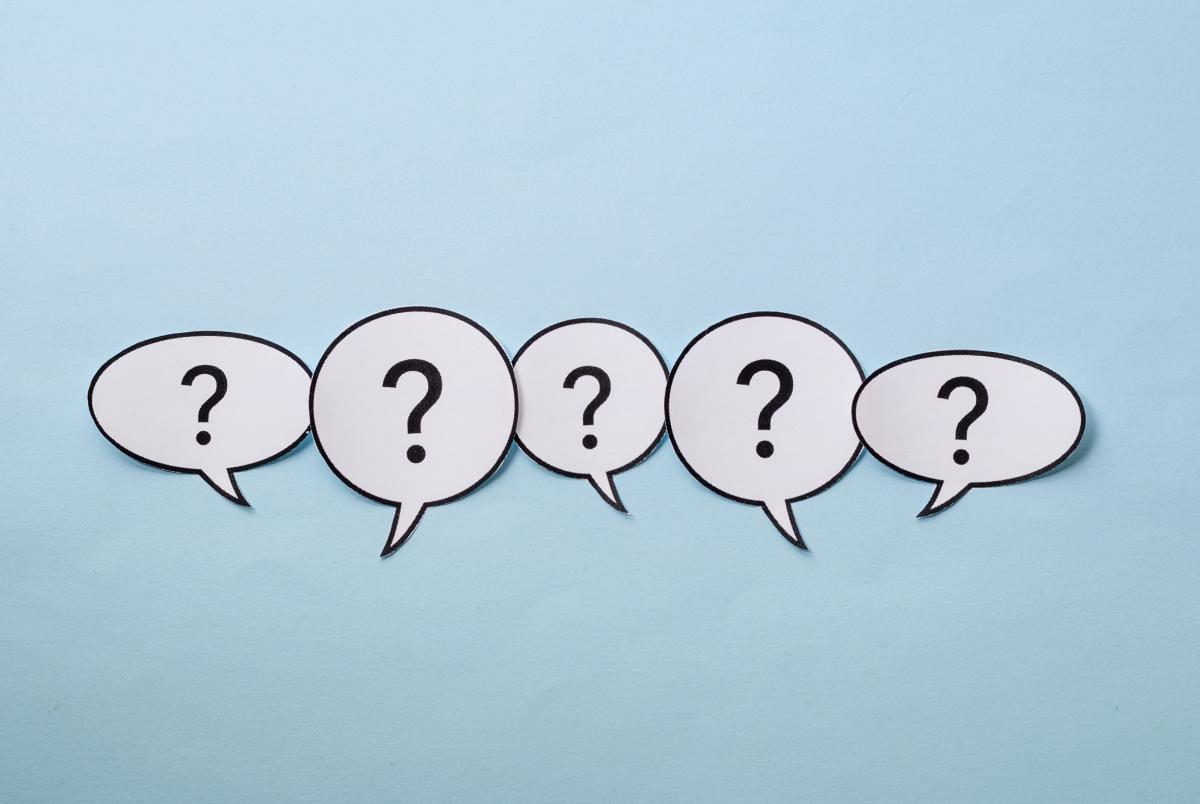 Paper speech bubbles with question marks inside them on a blue background.
